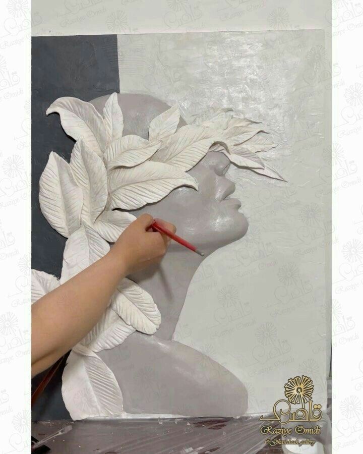 a person is painting a white statue with leaves on it's head and another hand holding a red brush