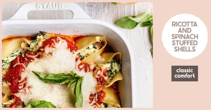 a white casserole dish filled with ravioli and spinach covered in sauce