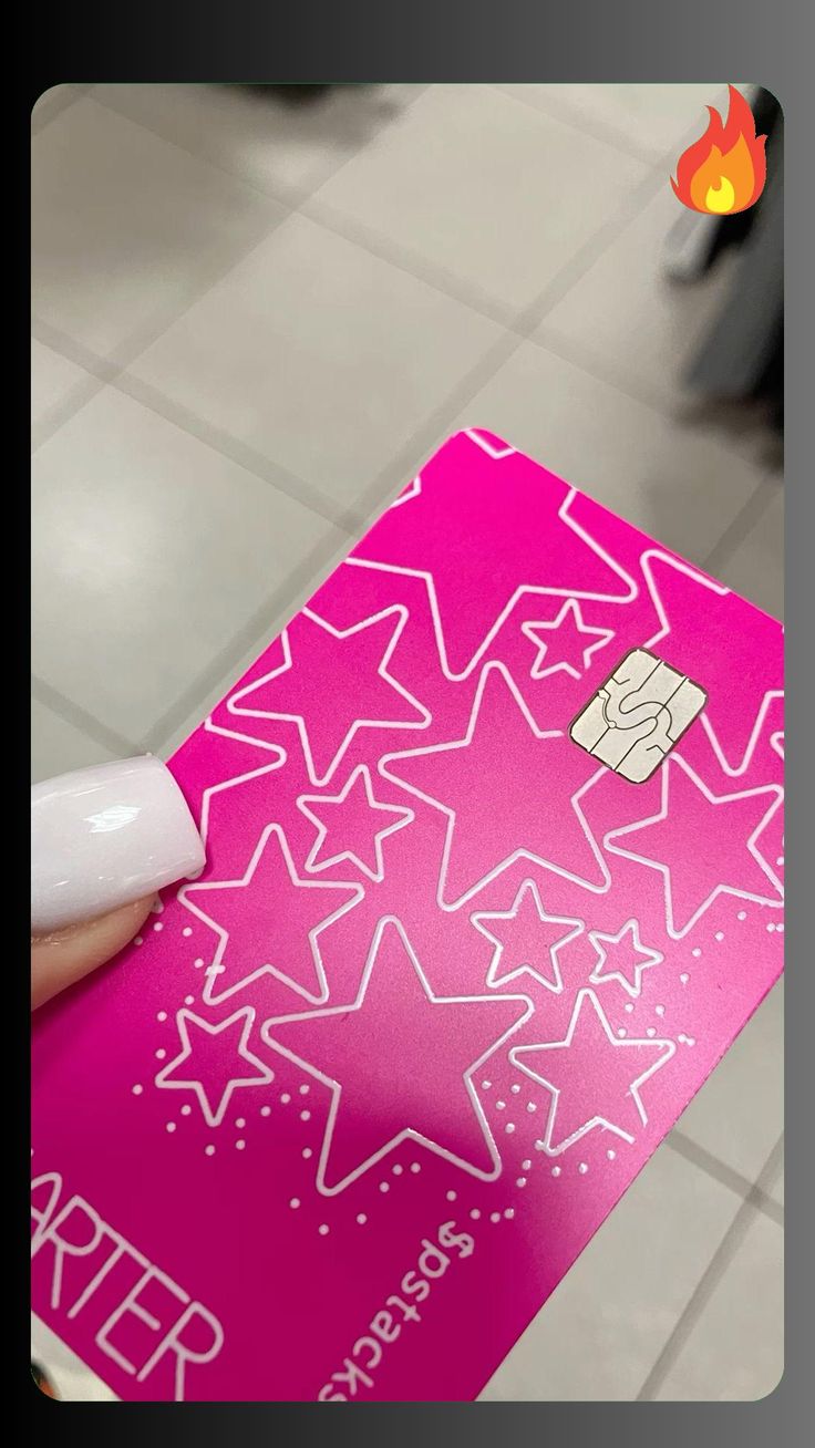 a hand holding a pink credit card with white stars on it and a red sticker