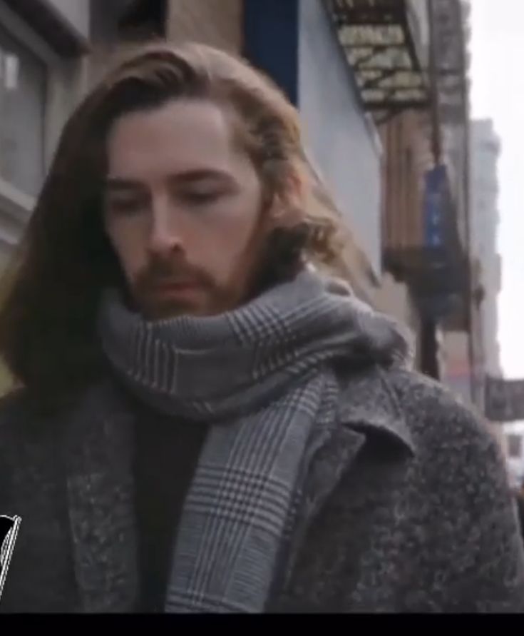 a man with long hair wearing a scarf on the street looking at his cell phone