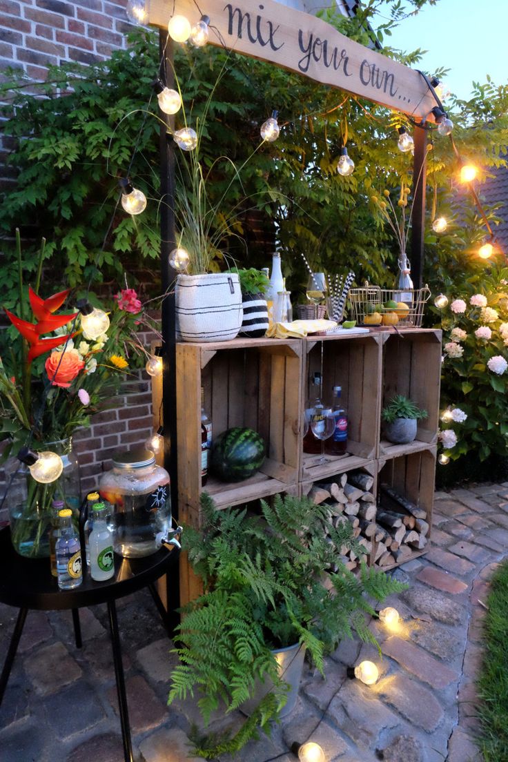 an outdoor bar with lots of plants and lights on the side of it, surrounded by greenery