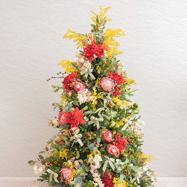 a small christmas tree decorated with flowers and greenery