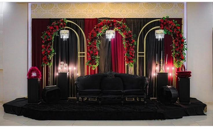 a stage set up with black couches and red roses on the wall, surrounded by candles