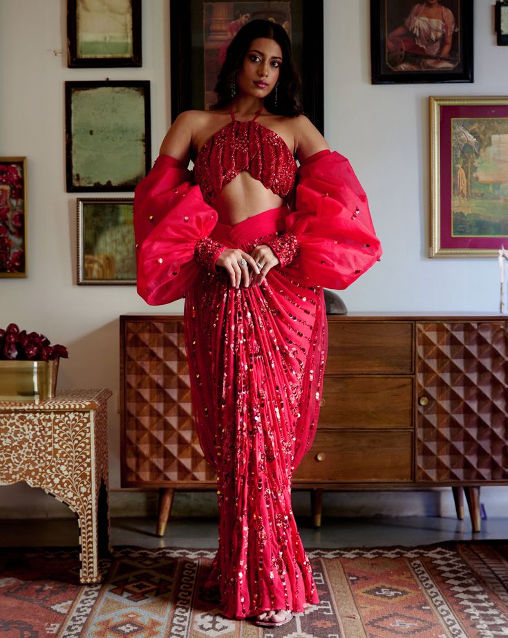 Step into iconic glamour where elegance is draped in the shimmer of scarlet palette for the season’s soirees. Our new-age concept of pre-draped saree features a chic halter neck blouse adorned with nalki crystals embellishment paired up with a sequined pre-draped skirt. Adding a hint of drama the handmade puffer sleeves complete the whole iconic look. • Pre-draped sequined skirt.• Halter-neck blouse adorned with nalki crystals and moti embellishments. • Metal hook at the back side of the blouse to conceal. • Puffed sleeves with an attached sequined dupatta.• Metal zip on the backside of the skirt along with a hook for support.From Moledro’s Fitoor collection. DELIVERY TIMEPlease allow 8-12 weeks for your outfit to arrive. FABRIC DETAILSBlouse: Butterfly Net Skirt: GeorgetteSleeves: Net Pro Festive Evening Pre-draped Saree With Zari Work, Elegant Pre-draped Saree For Party Season, Glamorous Lehenga For Gala Festivities, Glamorous Lehenga For Festive Gala, Elegant Fitted Pre-draped Saree For Party Season, Evening Party Wear Pre-draped Floor-length Saree, Glamorous Evening Lehenga With Traditional Drape, Festive Fitted Pre-draped Saree For Gala, Glamorous Festive Pre-draped Saree For Gala