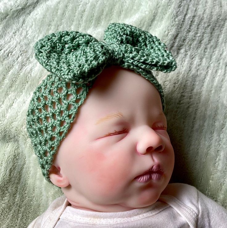 a baby wearing a green crocheted headband laying on top of a bed