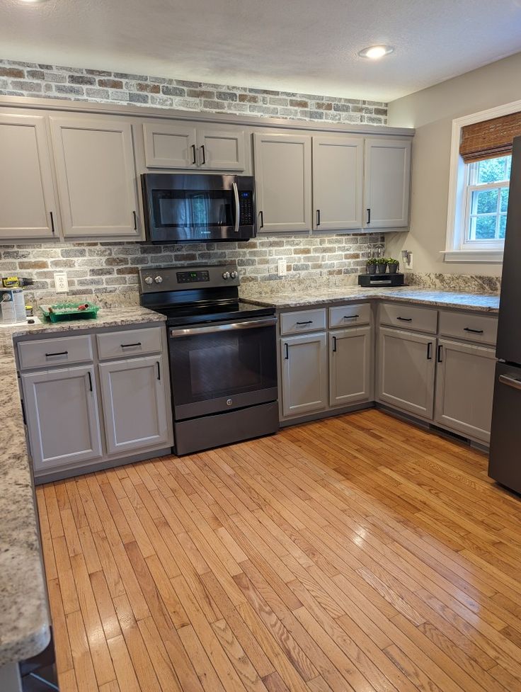 an empty kitchen with wood floors and gray cabinets in the center, along with stainless steel appliances