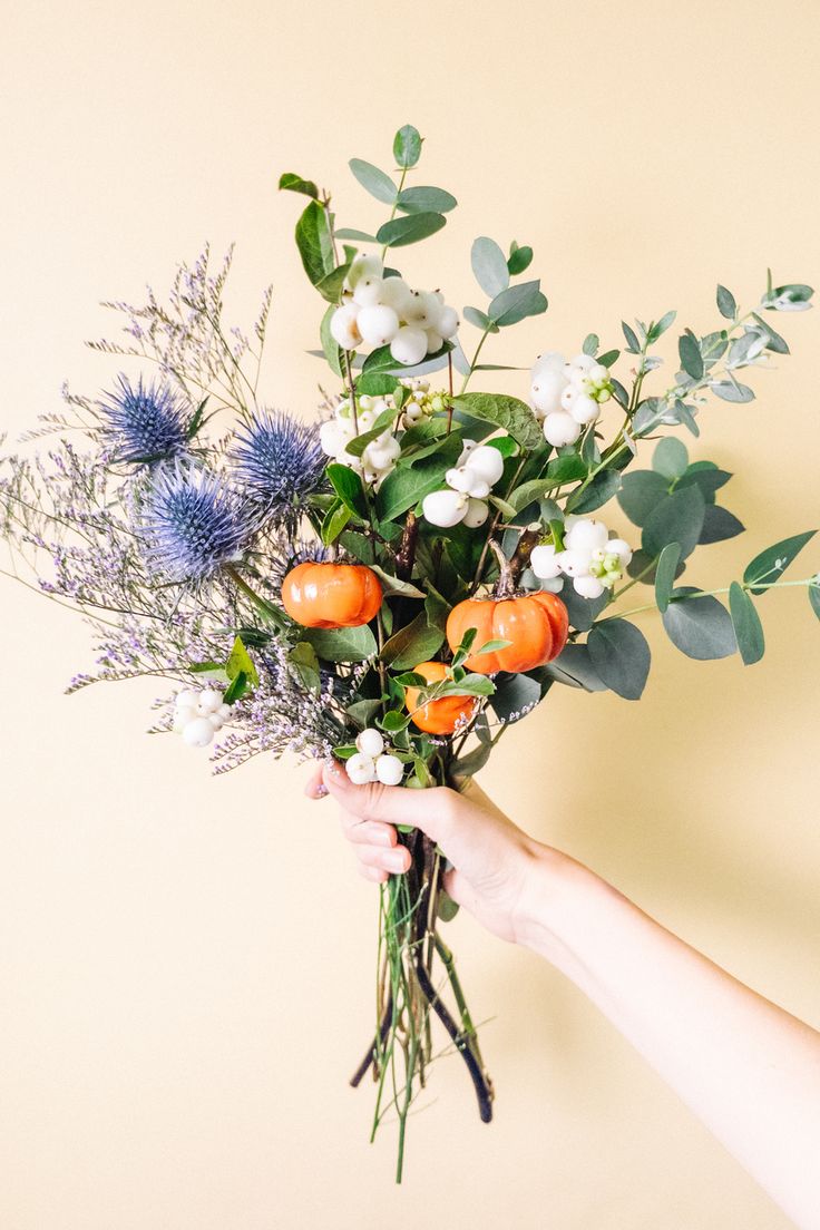 a person holding a bunch of flowers with oranges and blue berries on them,