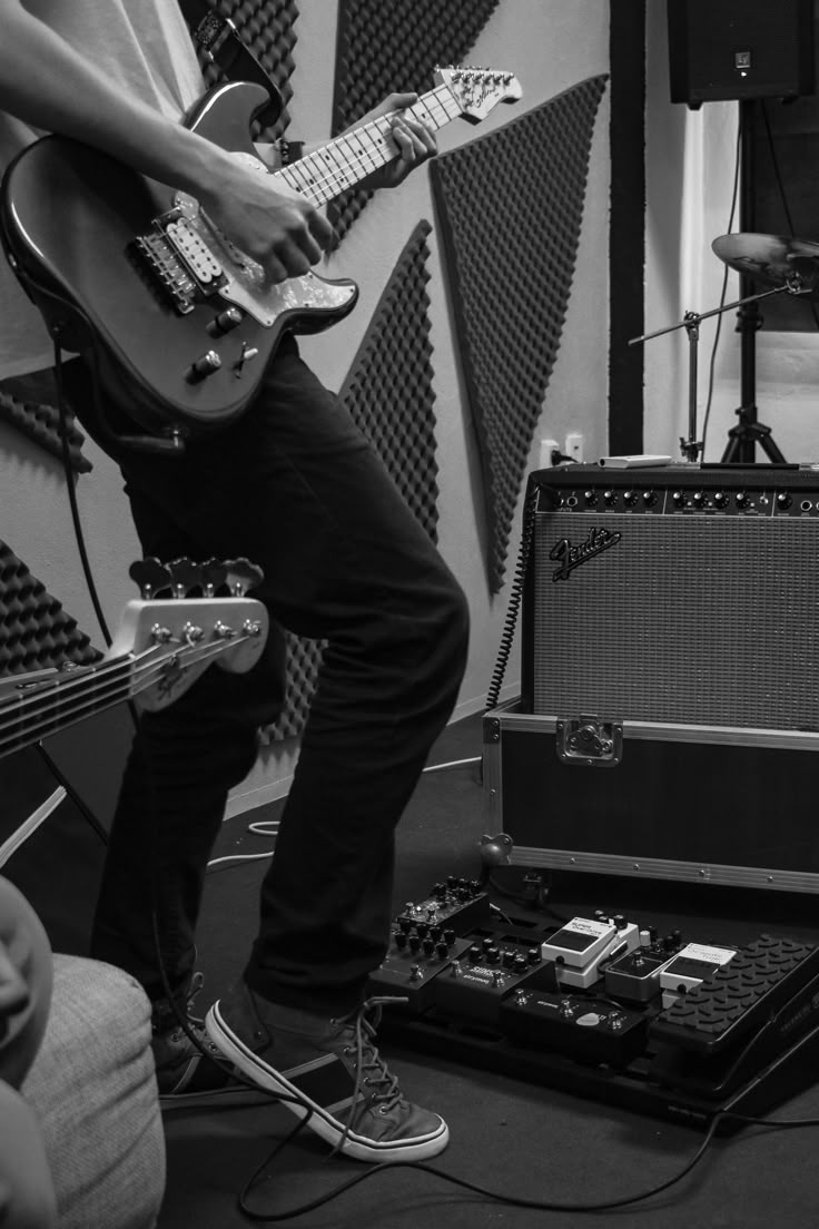 black and white photo of man playing guitar in recording studio with sound equipment behind him