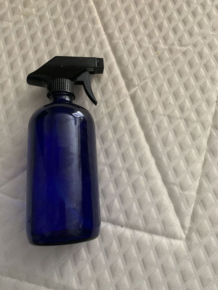 a blue spray bottle sitting on top of a white bed sheet with a black cap