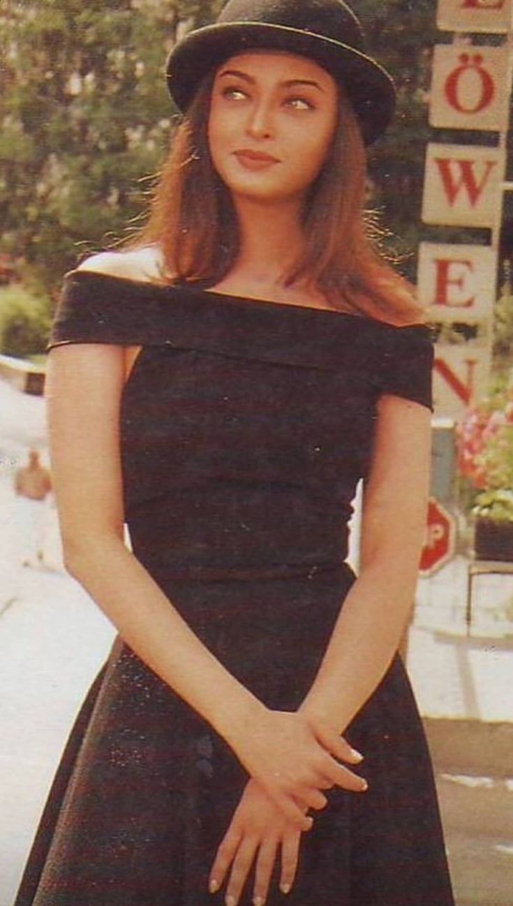 a woman in a black dress and hat posing for a photo