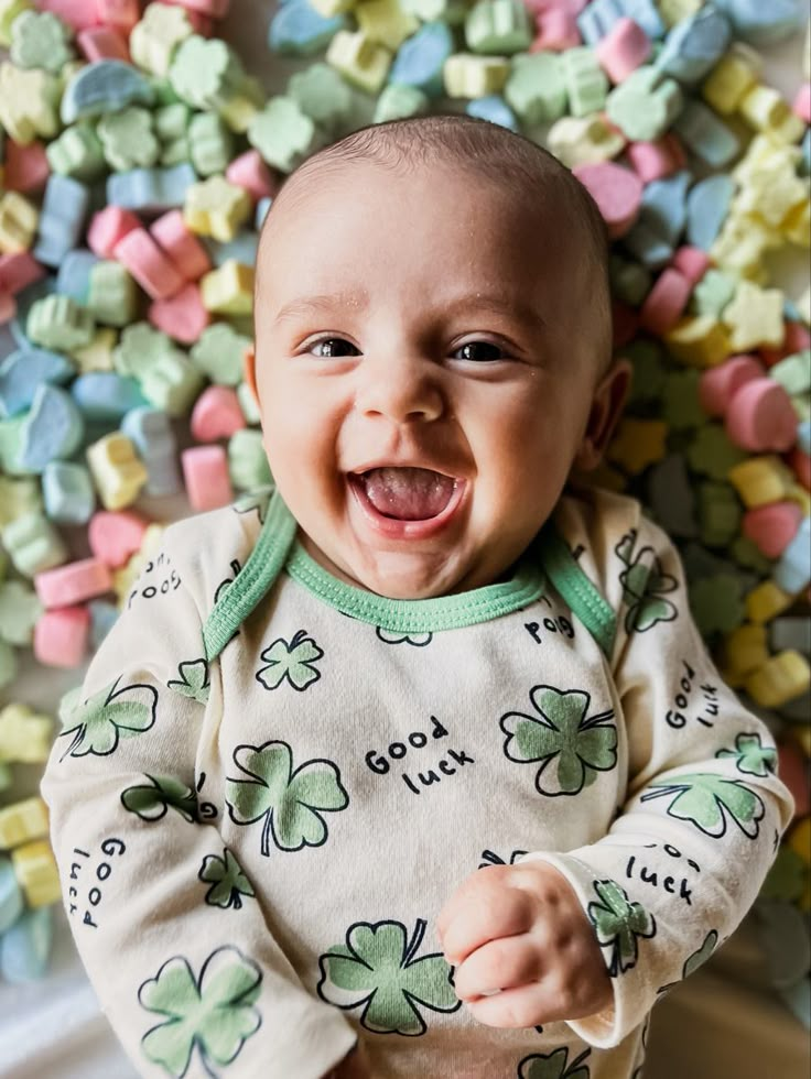 a baby is smiling and surrounded by marshmallows in his st patrick's day outfit