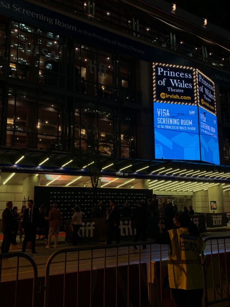 people are standing in front of a building with a large screen on it's side