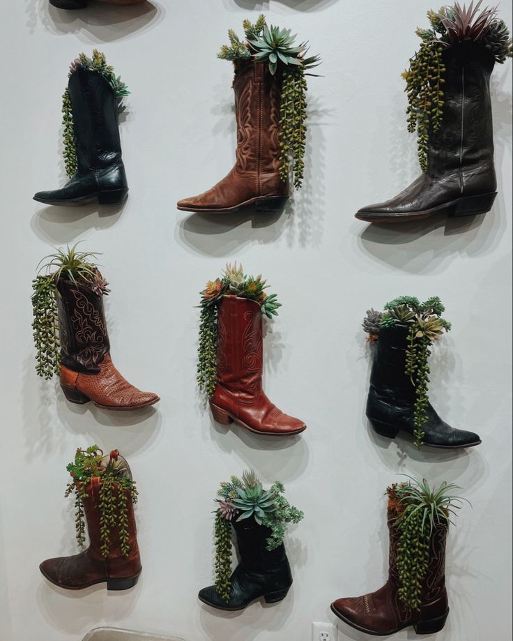 many different types of boots with plants growing on the sides and bottom, all hanging up against a white wall