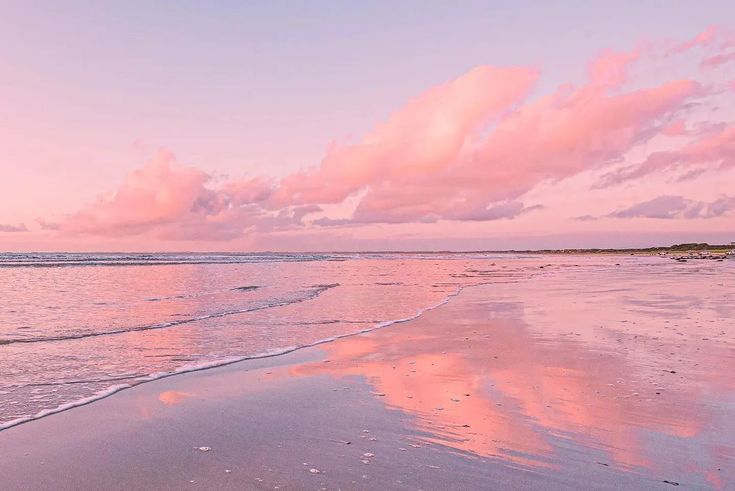 a beach with waves coming in to the shore and pink clouds above it at sunset