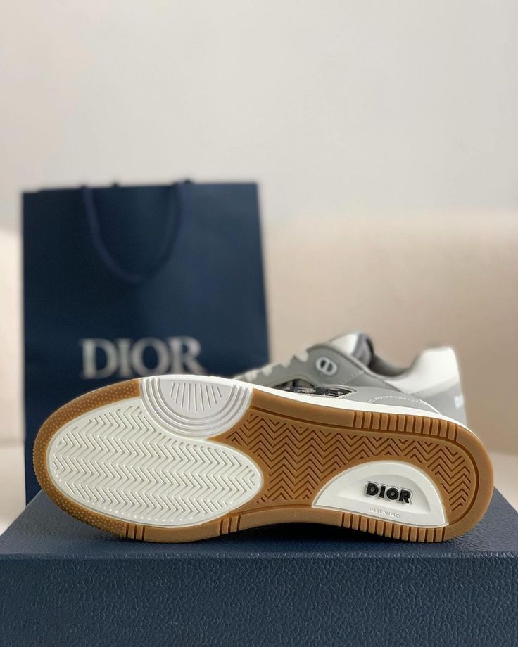 Embrace a blend of retro athleticism and modern luxury with these low-top sneakers, inspired by the iconic Dior B27. Featuring a sophisticated grey and white color scheme with subtle Dior Oblique-inspired accents, these shoes offer a refined and versatile look. Crafted with meticulous attention to detail, the smooth calfskin and patterned canvas upper create a textural contrast, while the perforated toe box ensures breathability. The signature "DIOR" branding adds a touch of high-fashion appeal. Luxury Gray Lace-up Sneakers, Designer Gray Sneakers With Round Toe, Luxury Gray Sneakers With Round Toe, Luxury Gray Round Toe Sneakers, Gray Low-top Sneakers With Branded Heel Counter, Designer Gray Lace-up Sneakers, Dior Branding, Dior Oblique, Loafer Sneakers