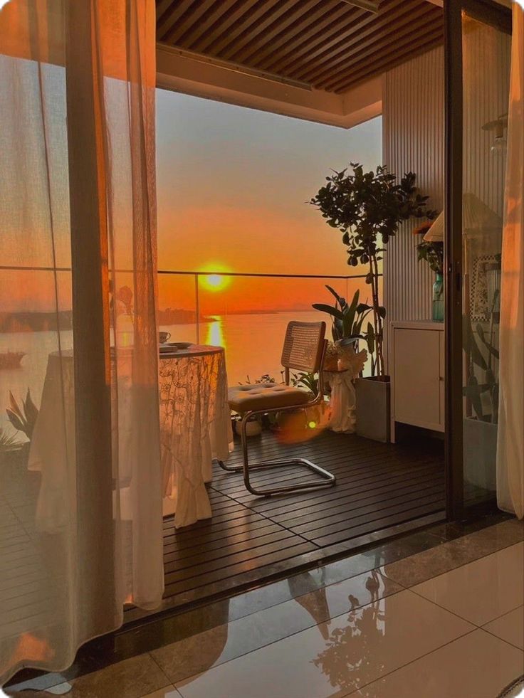 the sun is setting over the water from an open balcony with chairs and plants on it