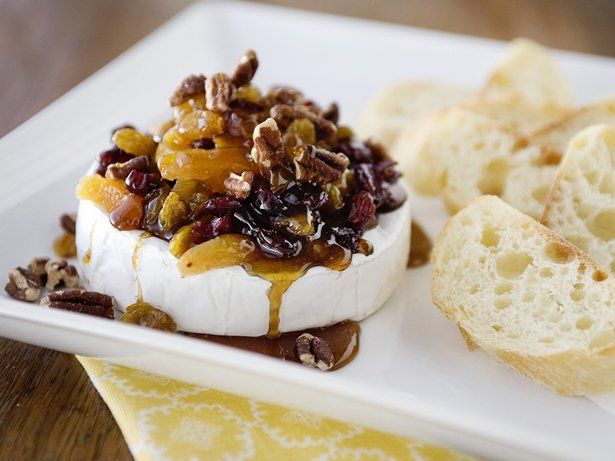 a white plate topped with cheese covered in nuts and raisins next to slices of bread