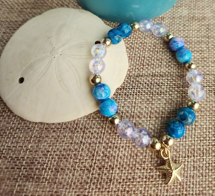 Elegant 7-inch bracelet made to fit most adult women.  Delicate golden starfish charm hangs from turquoise blue and iridescent bracelet. Adjustable Blue Bracelets With Starfish Charm, Adjustable Blue Jewelry With Starfish Charm, Adjustable Blue Starfish Jewelry, Blue Bracelet With Starfish Charm And Round Beads, Blue Bracelets With Starfish Charm And Round Beads, Turquoise Beaded Bracelets With Starfish Charm, Turquoise Ocean-inspired Bracelet With Starfish Charm, Ocean-inspired Turquoise Bracelet With Starfish Charm, Blue Beaded Bracelet With Starfish Charm