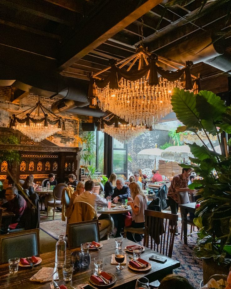 people sitting at tables in a restaurant with chandeliers hanging from the ceiling