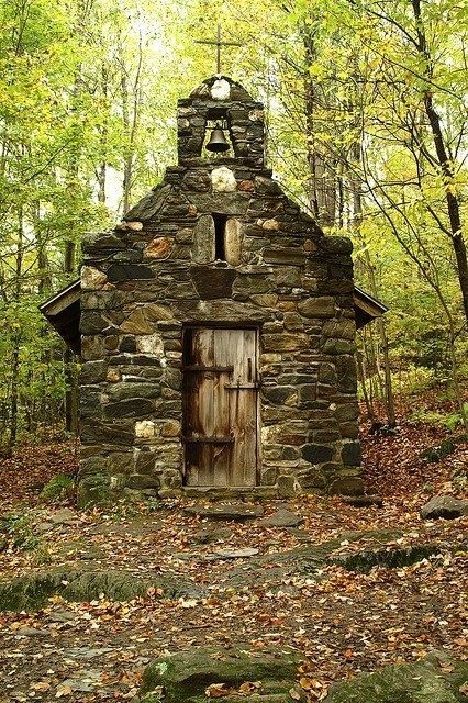 an old stone building in the woods with leaves on the ground and trees around it