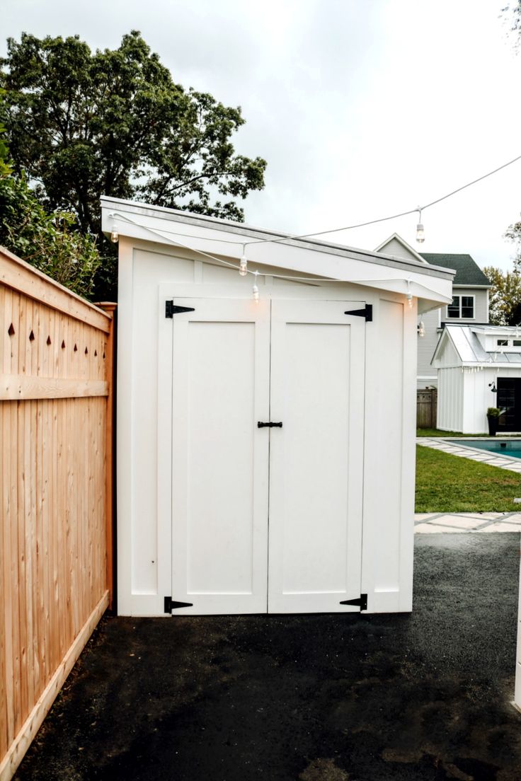 a white storage shed next to a wooden fence