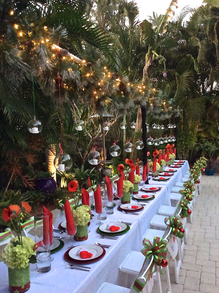 a long table is set up with red and green place settings for an outdoor dinner