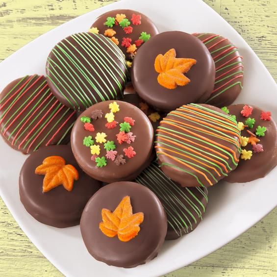 chocolate covered candies are arranged on a white plate with autumn leaves and candy sprinkles