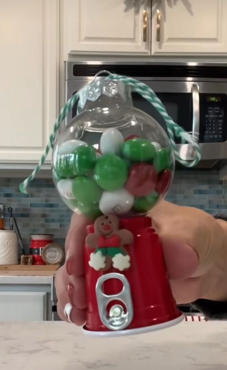 a person is holding up a christmas ornament in the kitchen with candy on it