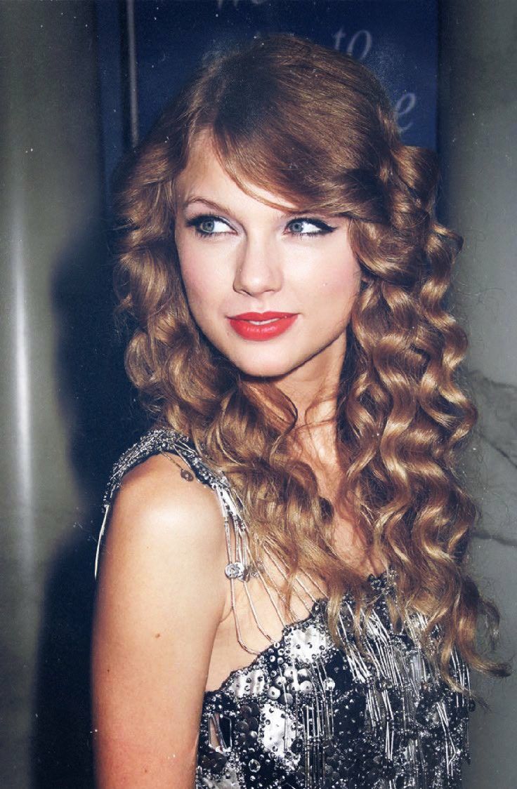 a beautiful young lady with long curly hair and red lipstick posing for the camera in front of a blue sign