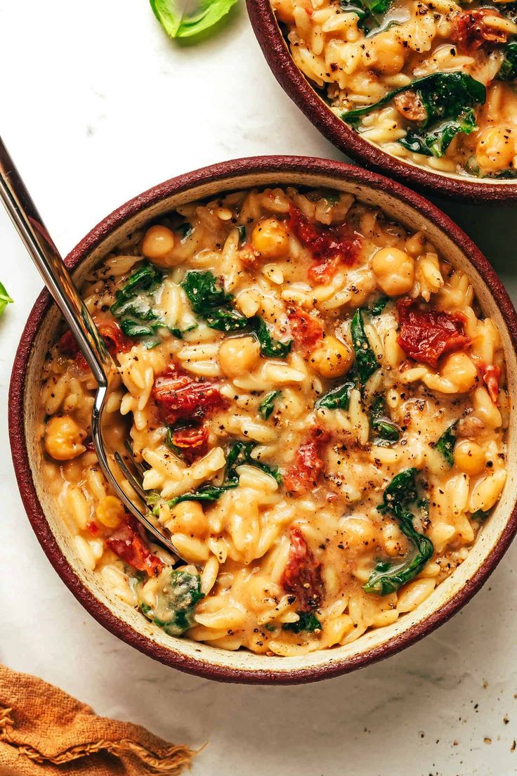 two bowls filled with pasta and spinach on top of a white table next to a spoon