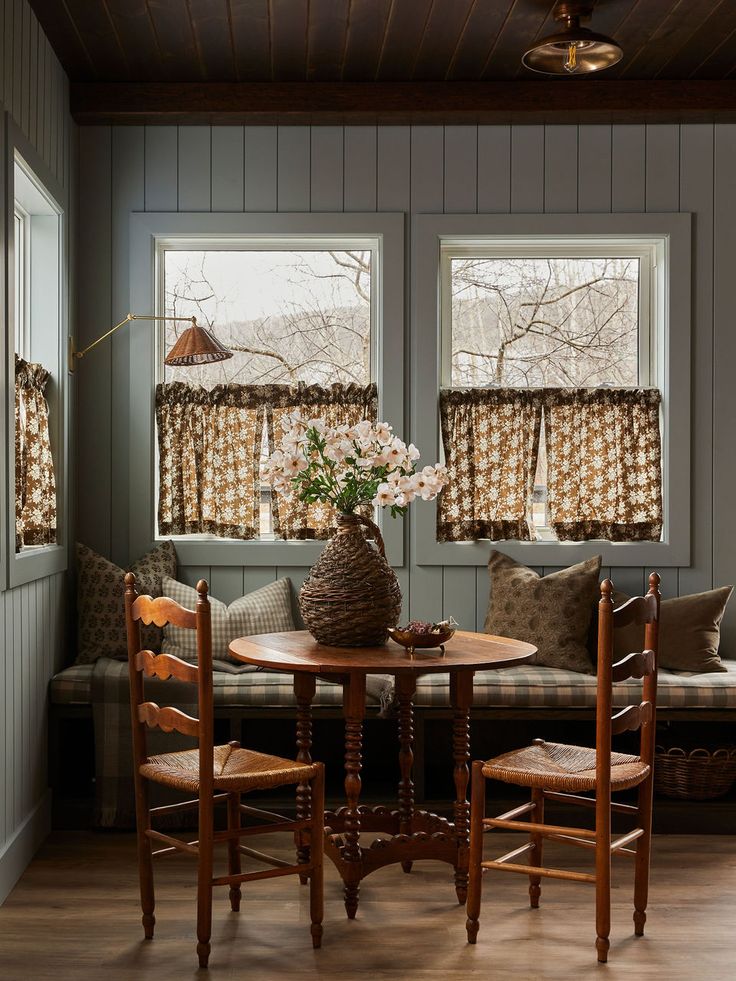 a table and chairs in a small room with two windows above the couch, next to a window seat