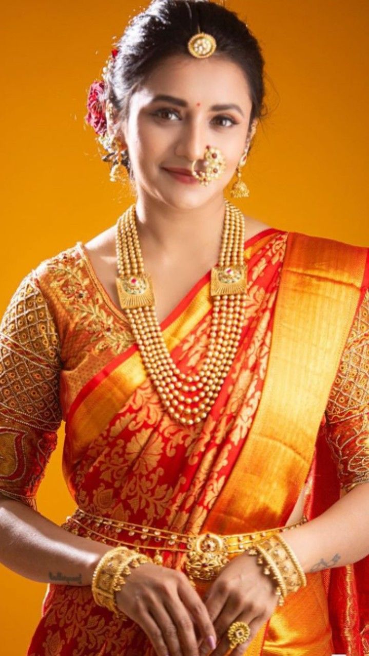 a woman in an orange and red sari with gold jewelry on her neck, standing against