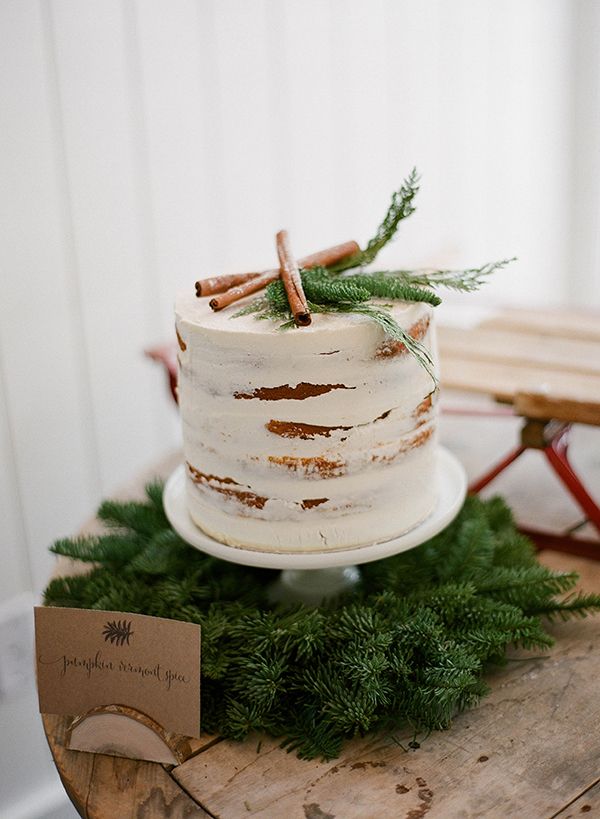 a white cake sitting on top of a wooden table covered in greenery and cinnamon sticks