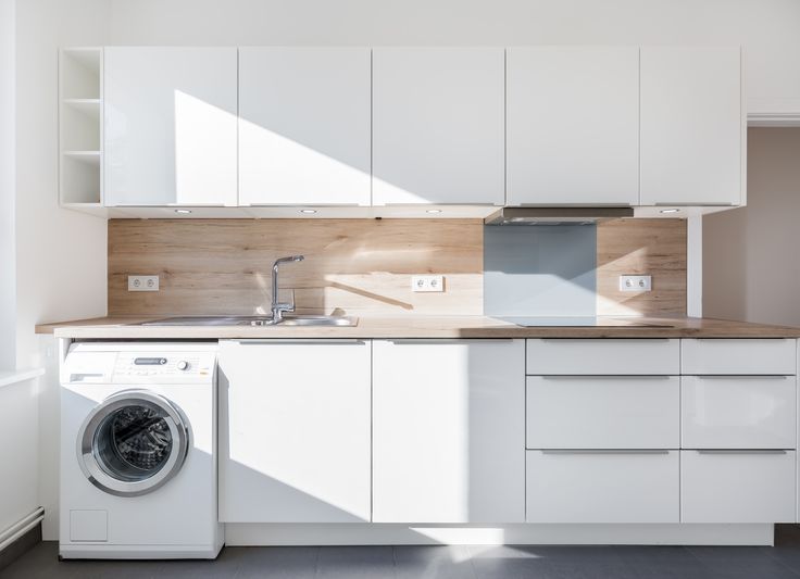 a washer and dryer in a white kitchen with wooden counter tops on the side