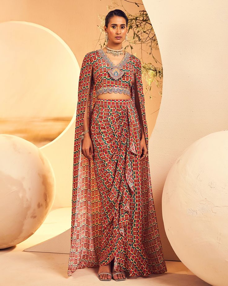 Featuring a ruffe pickup skirt with a cape blouse in a classic Asian ikat print. The neckline has mirror and sequin embroidery which is accentuated with ruby and emerald-coloured stones and pearls. From Aneesh Agarwaal's Naksh collection. DELIVERY TIMEPlease allow 8-12 weeks for your outfit to arrive. FABRIC DETAILSCrepe Professional cleaning only. Traditional Multicolor Sets With Cape Sleeves, Bohemian Party Sets With Cape Sleeves, Bohemian Fitted Sets With Cape Sleeves, Designer Red Ruffled Sets, Bohemian Sequined Sets With Traditional Drape, Bohemian Ikat Print Choli For Festive Occasions, Traditional Choli With Cape Sleeves And Sequins, Traditional Choli With Sequins And Cape Sleeves, Traditional Sequin Dress With Cape Sleeves