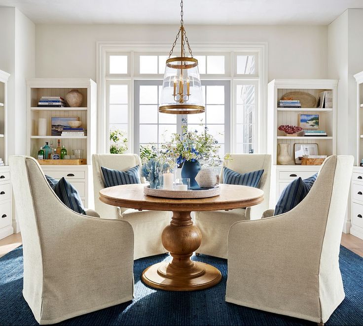 a dining room with chairs and a table in front of a large window that has built - in bookshelves