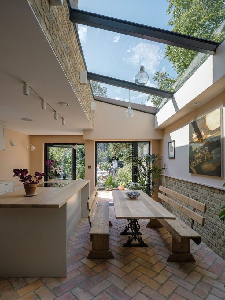 a kitchen area with a table, bench and glass roof over looking the garden outside