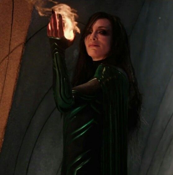 a woman dressed in black holding a fireball up to her face while standing next to a wall