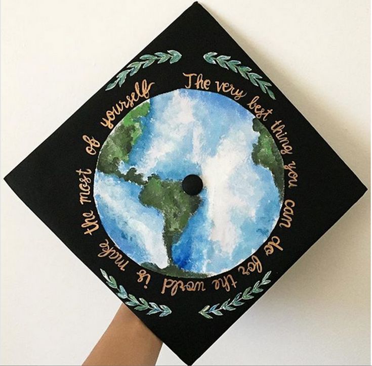 a hand holding a graduation cap with the earth painted on it's front and side