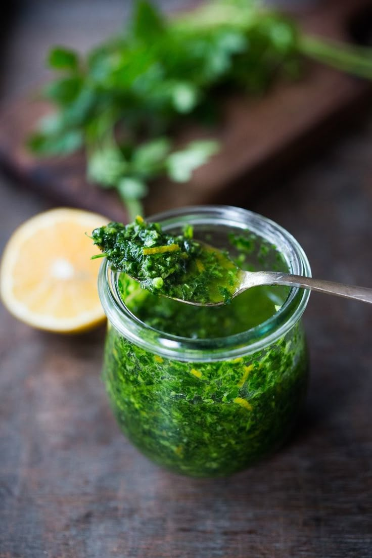 a jar filled with green liquid next to a lemon and parsley