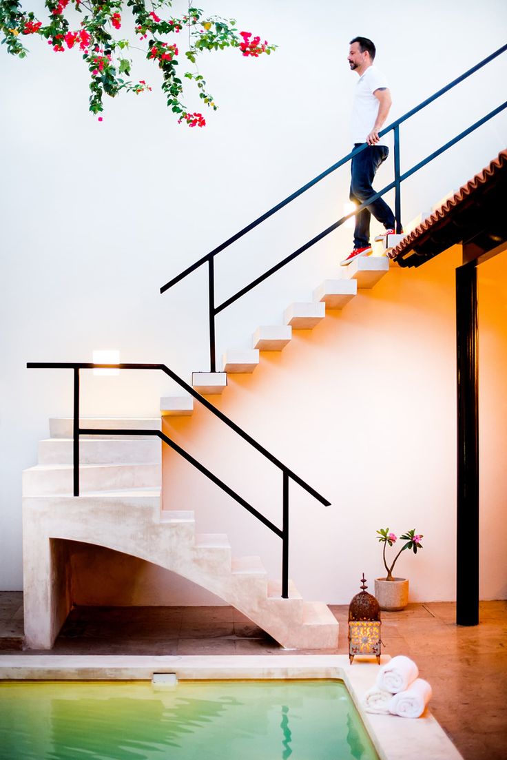 a man standing on top of a set of stairs next to a swimming pool in front of a white wall