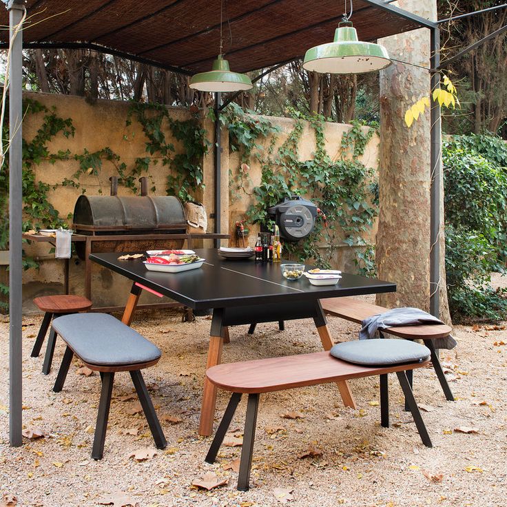 an outdoor table and benches under a covered area with lights hanging from the ceiling over it