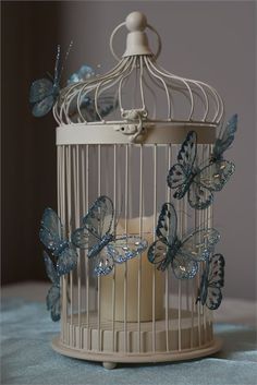 a white birdcage with blue butterflies on the top and bottom, sitting on a table