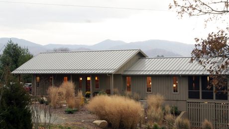 a house on the side of a hill surrounded by trees and bushes with mountains in the background