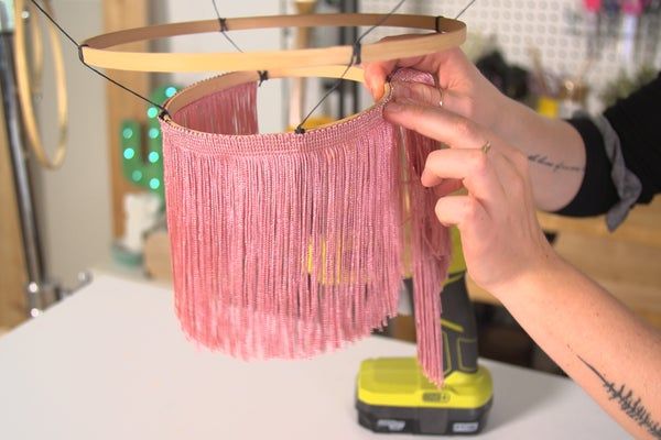 a woman is working on a project with pink yarn and wood beads hanging from it