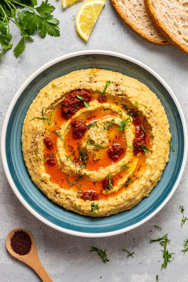 hummus in a bowl with bread and parsley on the side, ready to be eaten