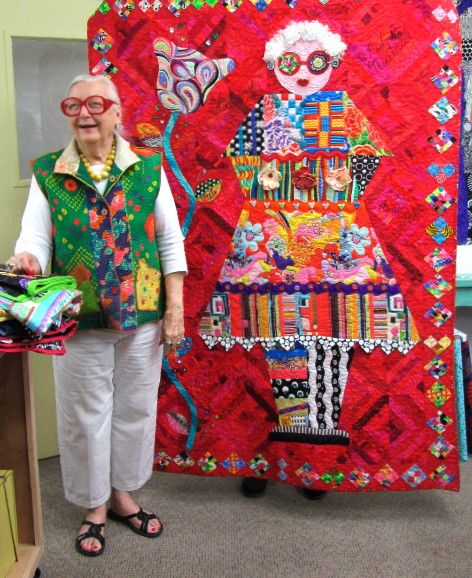 an older woman standing in front of a quilt