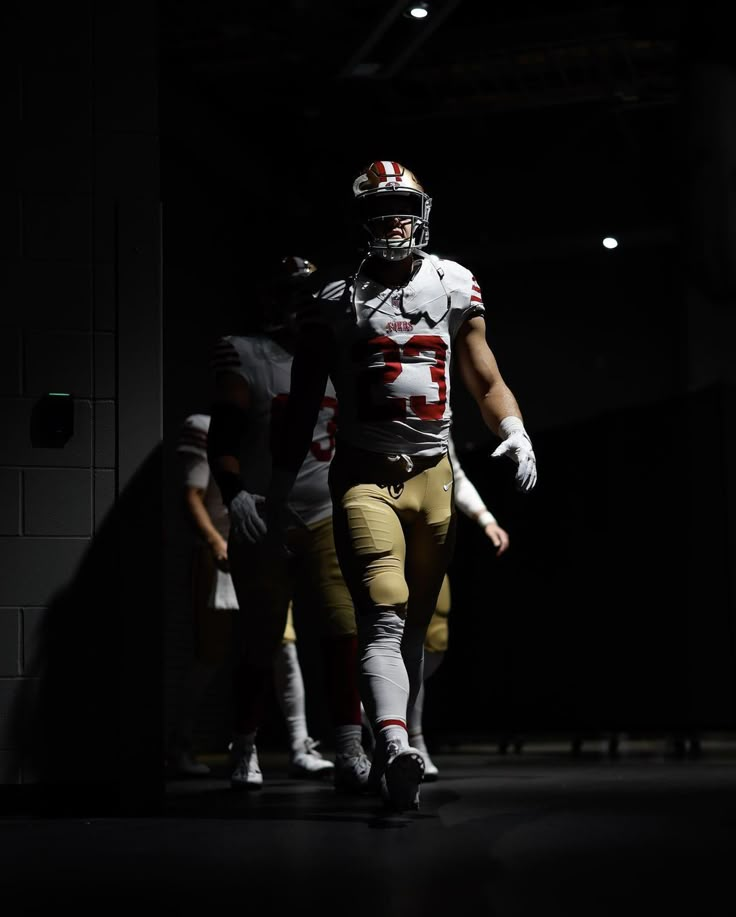 a football player is walking down the field at night with other players in the background