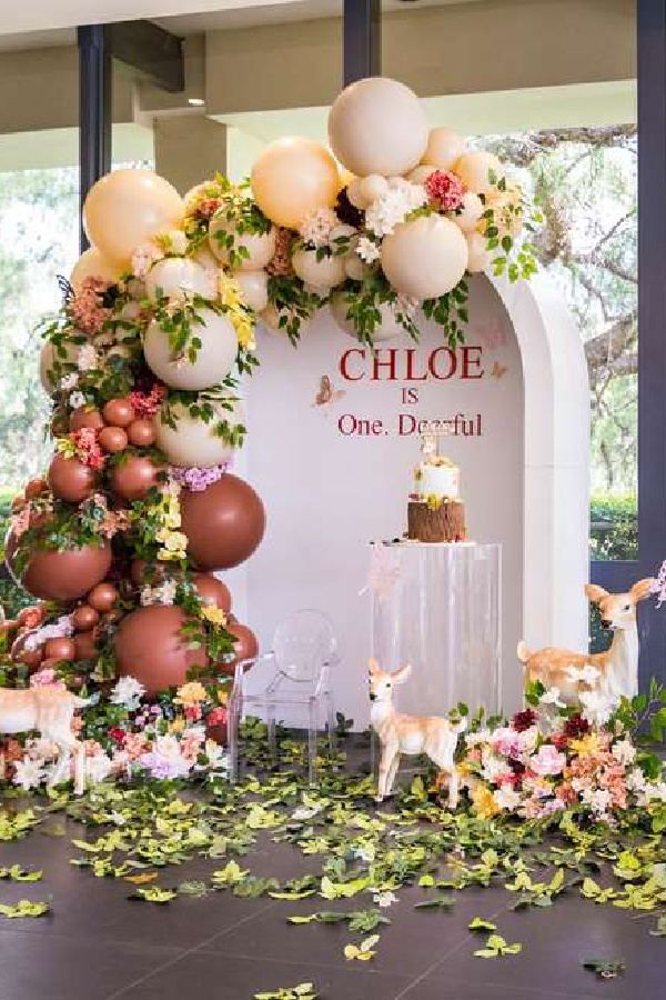 a wedding cake surrounded by balloons and flowers on the ground with deer figurines