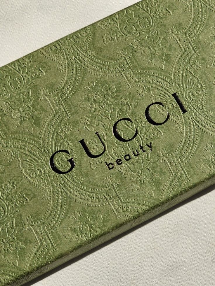 the gucci beauty box is sitting on top of a white tablecloth with an ornate pattern